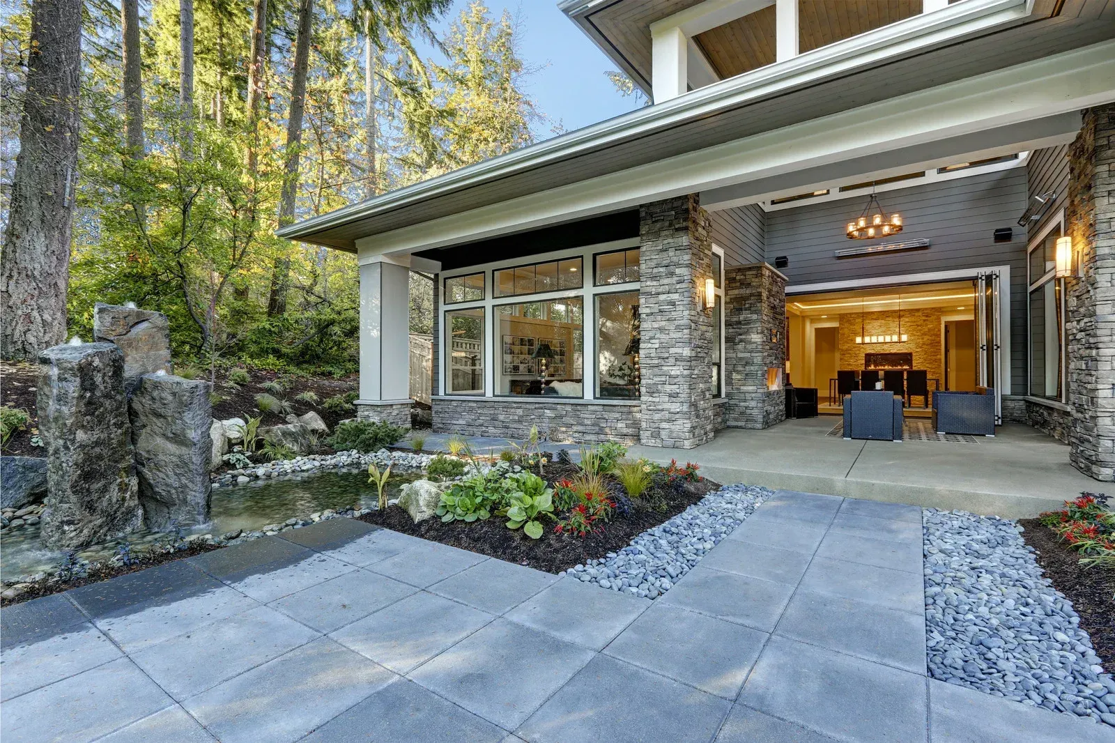 Modern home exterior with stone facade, patio, and lush landscaping.