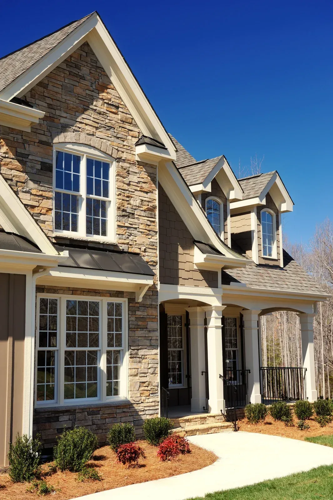 Stone and siding house with white trim and a porch, under a blue sky.