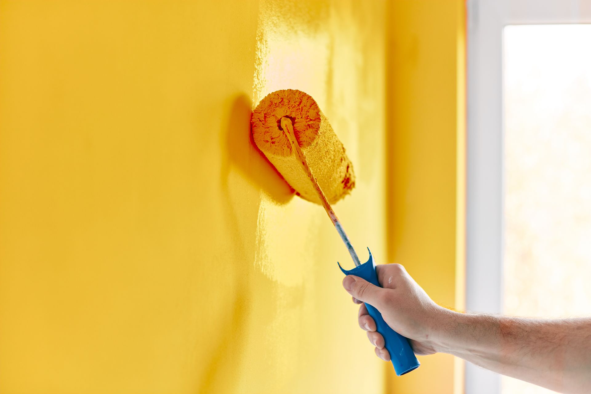 A person is painting a yellow wall with a paint roller.