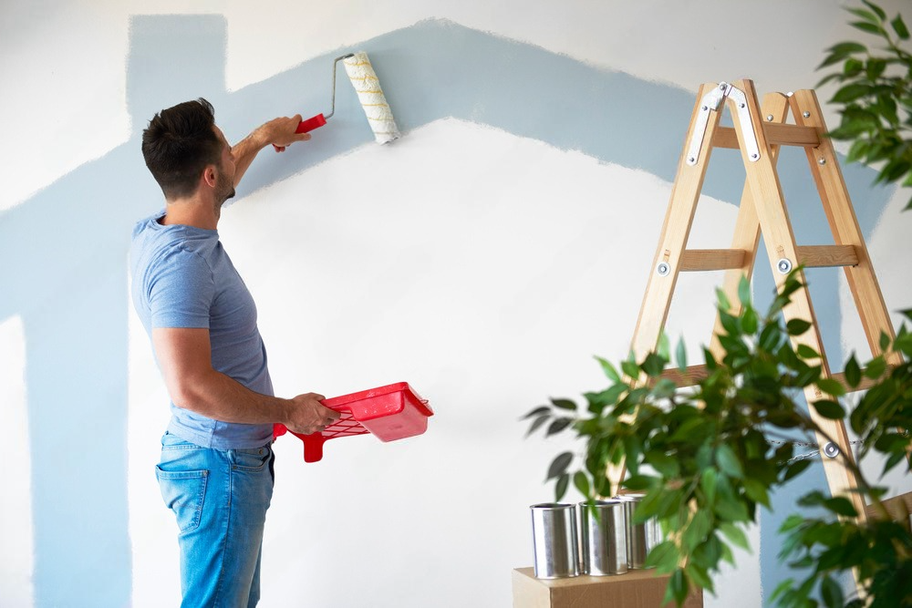 A man is painting a wall with a paint roller.