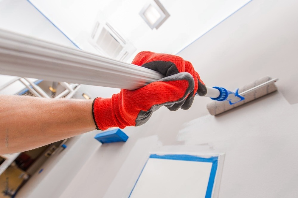 A person wearing red gloves is painting a wall with a paint roller.