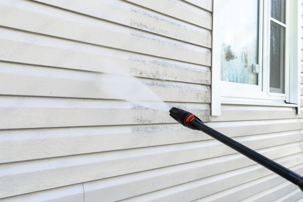 A person is cleaning the side of a house with a high pressure washer.