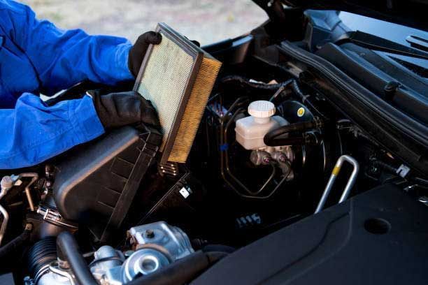 A person is holding a filter in their hand under the hood of a car.
