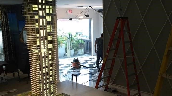 A man is standing next to a ladder in a room with a model of a building