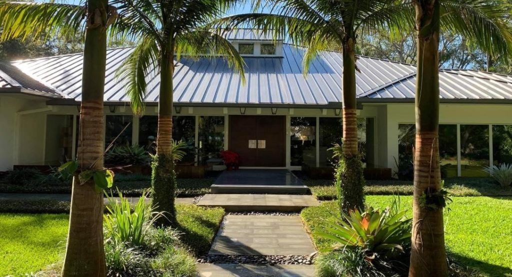 A large white house with a metal roof and palm trees in front of it