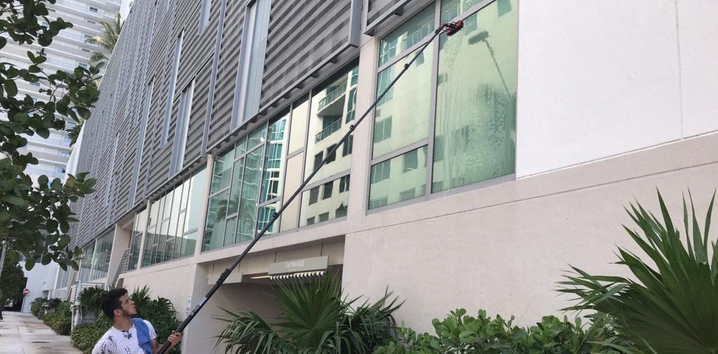 A man is cleaning the windows of a building with a long pole