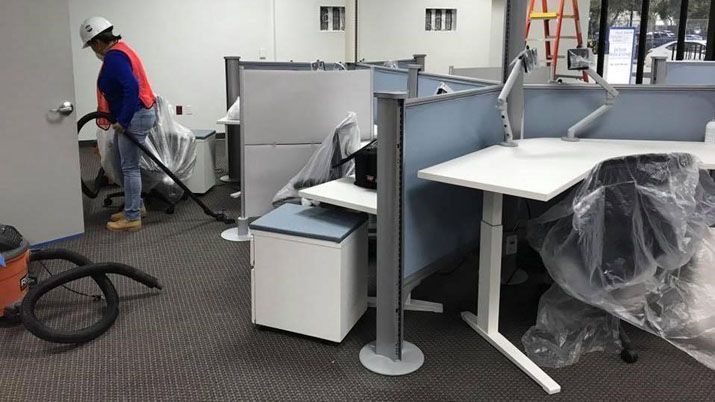 A man is cleaning the floor of an office with a vacuum cleaner