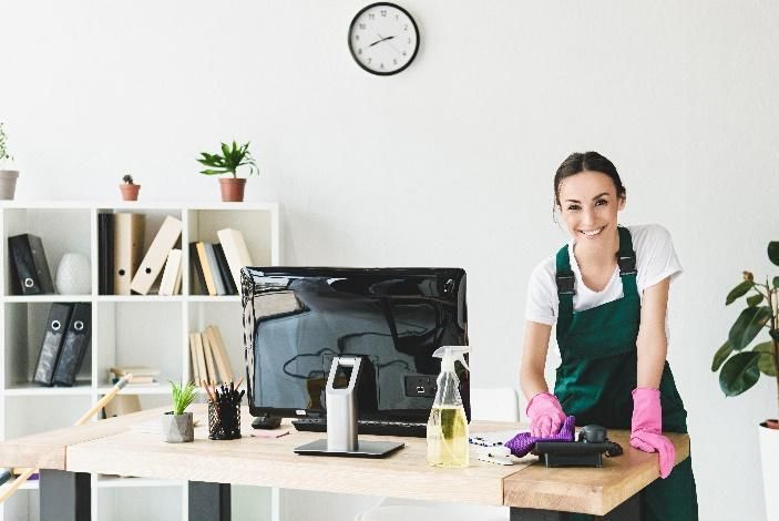 A woman is cleaning an office desk with a computer on it