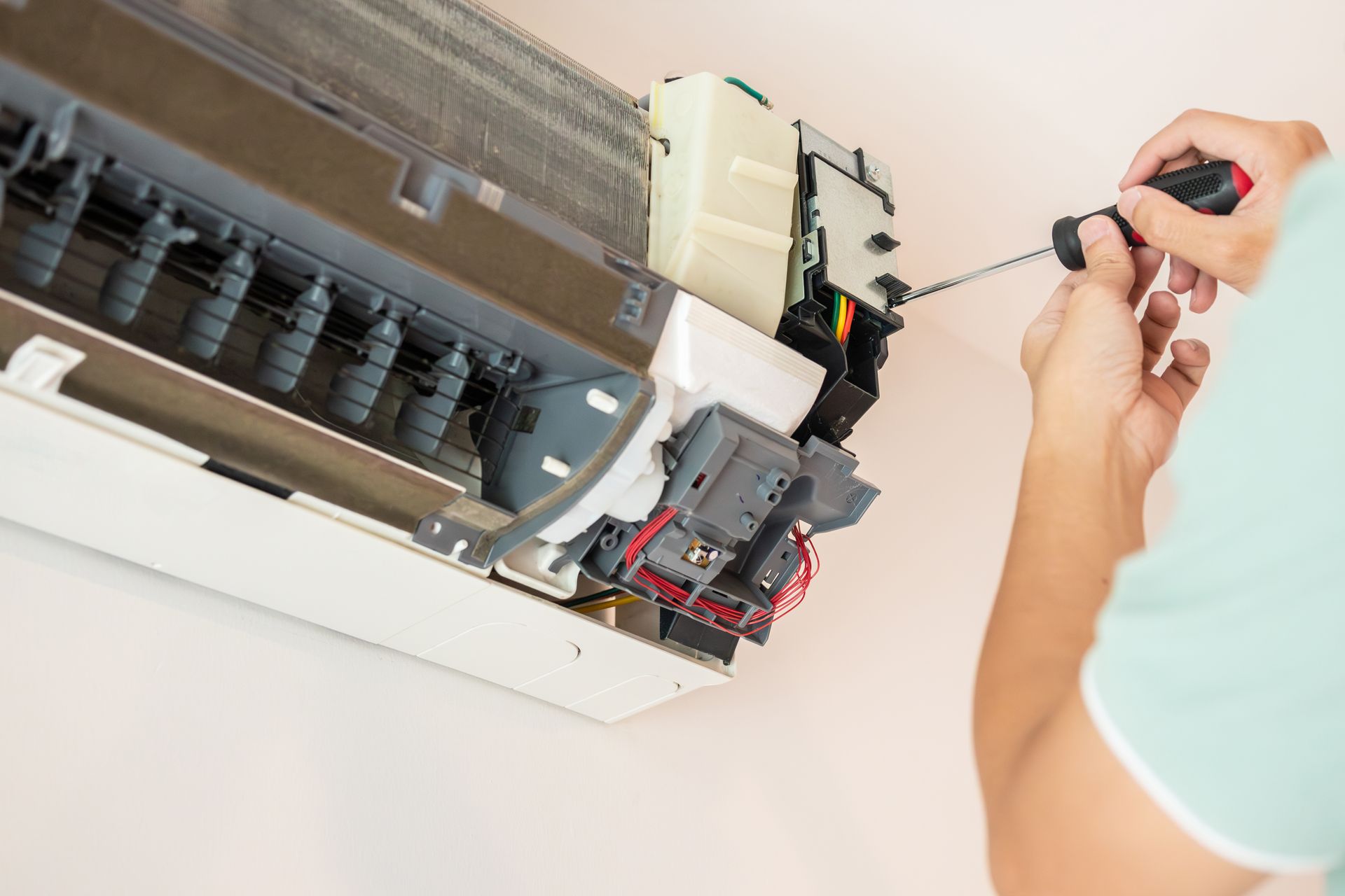 Person using a screwdriver to repair a white wall-mounted air conditioner.