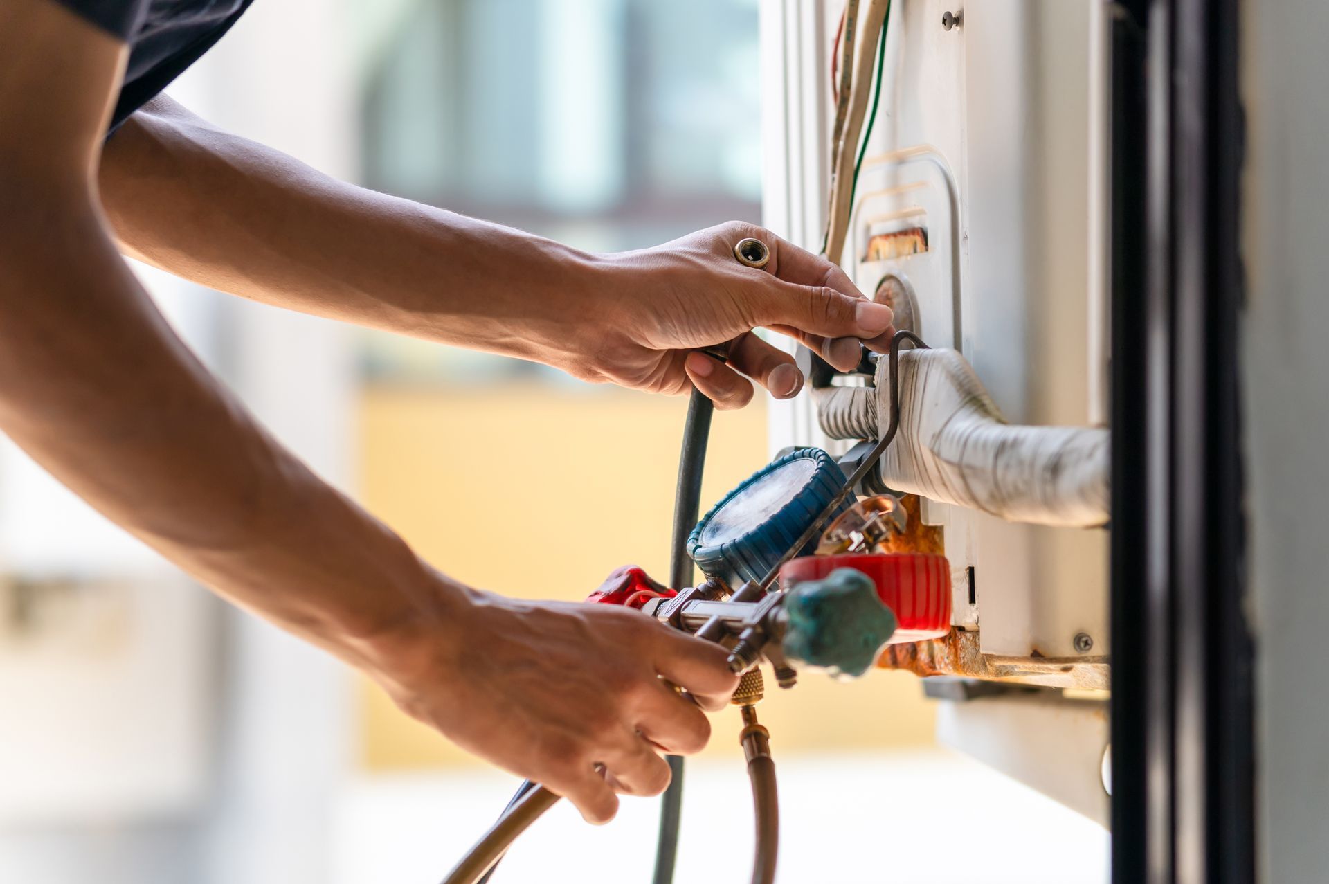 A person connecting gauges to an outdoor air conditioning unit for servicing.