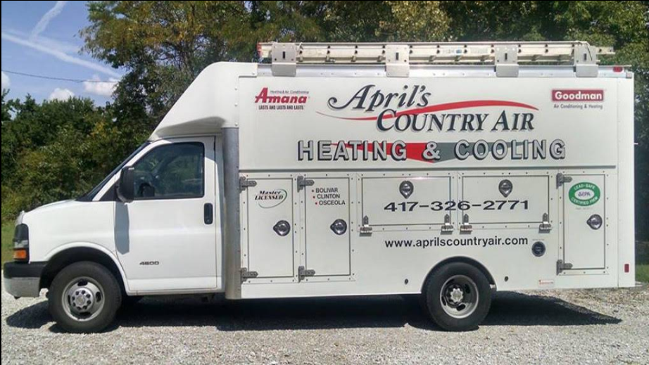 Three air conditioning units outside a white house with brown shutters, next to a concrete border and green grass.