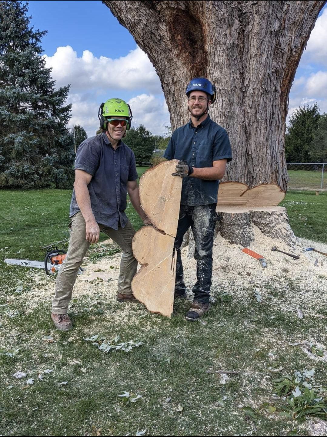 Two men are standing next to a tree holding a piece of wood.