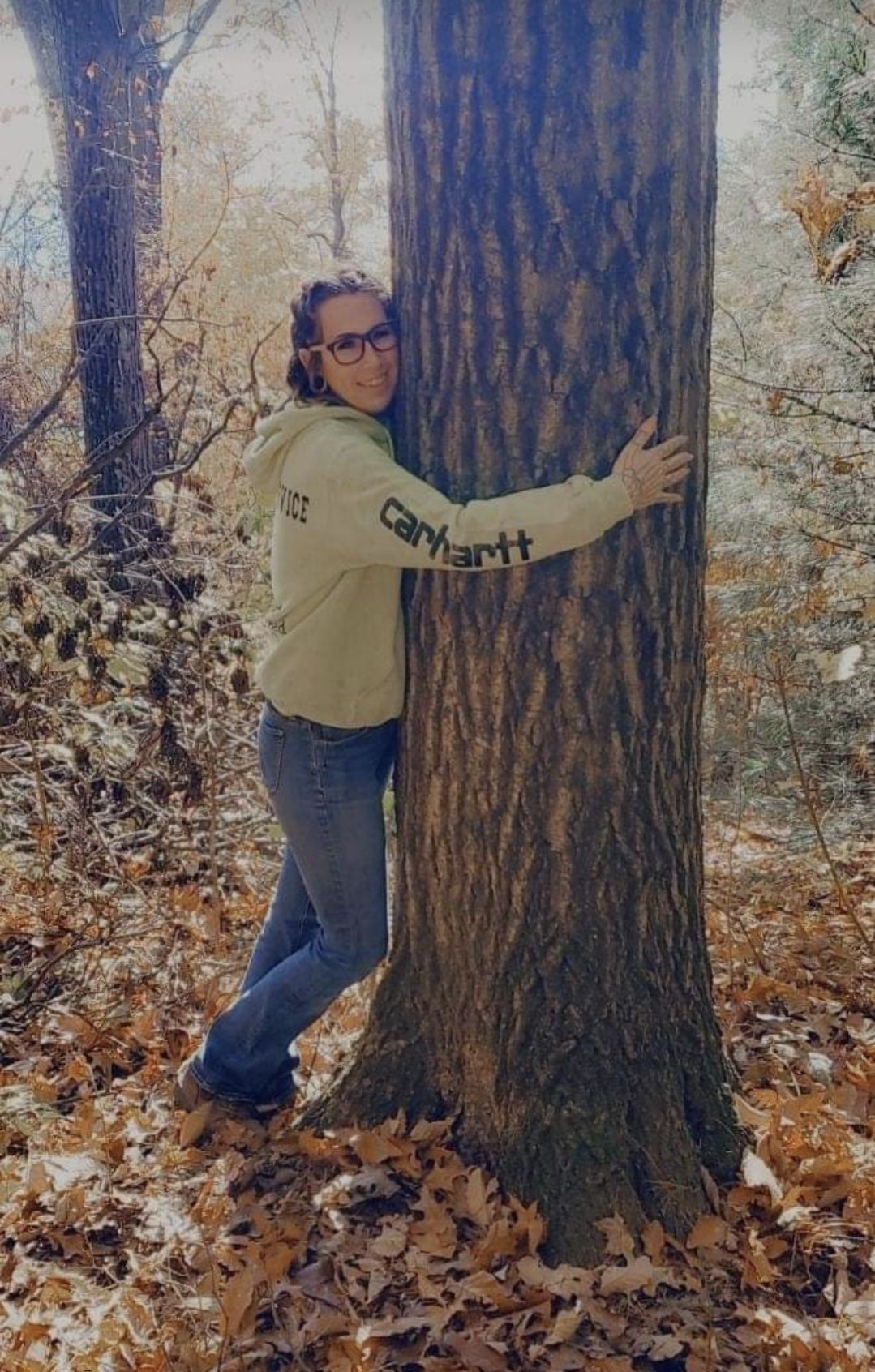 A woman is hugging a tree in the woods.