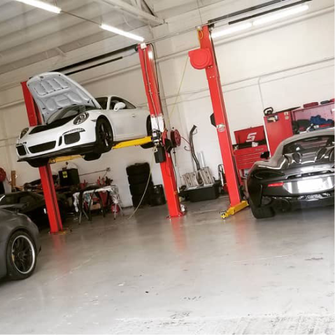 White Porsche raised on a lift in a garage, a black car to the side. Red lift and tool cabinet. | The Garage