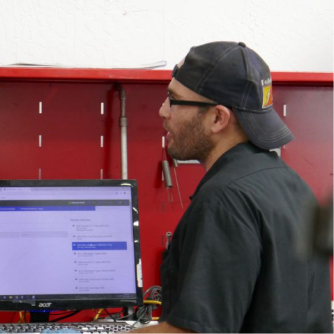 Man wearing a cap and glasses looking at a computer monitor in a red workshop setting. | The Garage