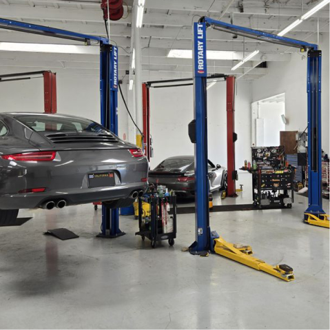 A gray car on a lift in a garage with other cars and equipment. |The Garage