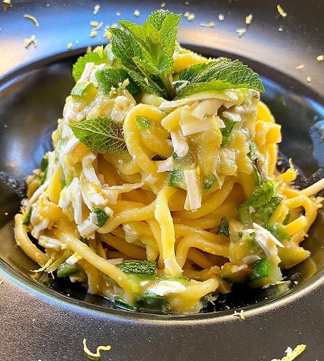 Piatto di pasta in una ciotola nera, guarnito con menta e scorza di limone.