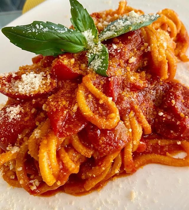 Spaghetti con salsa di pomodoro, basilico e parmigiano grattugiato su un piatto bianco.