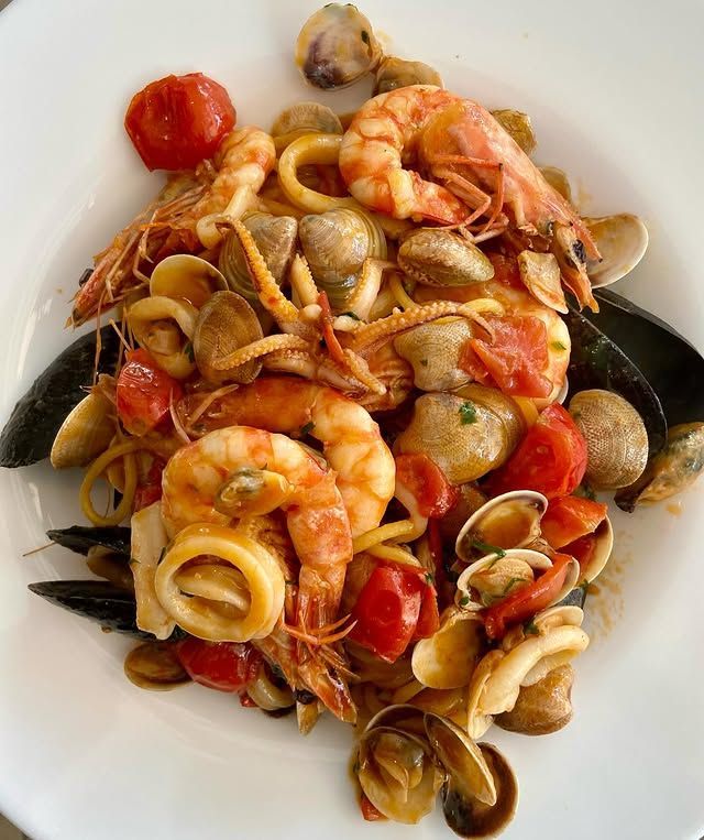 Piatto di pasta con gamberi, vongole, cozze, calamari e pomodori.