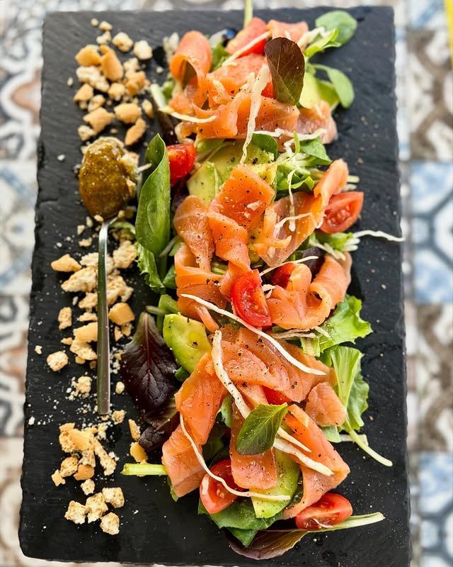 Insalata di salmone su una lavagna nera, con verdure, pomodori, avocado e crostini; un cucchiaio di salsa.
