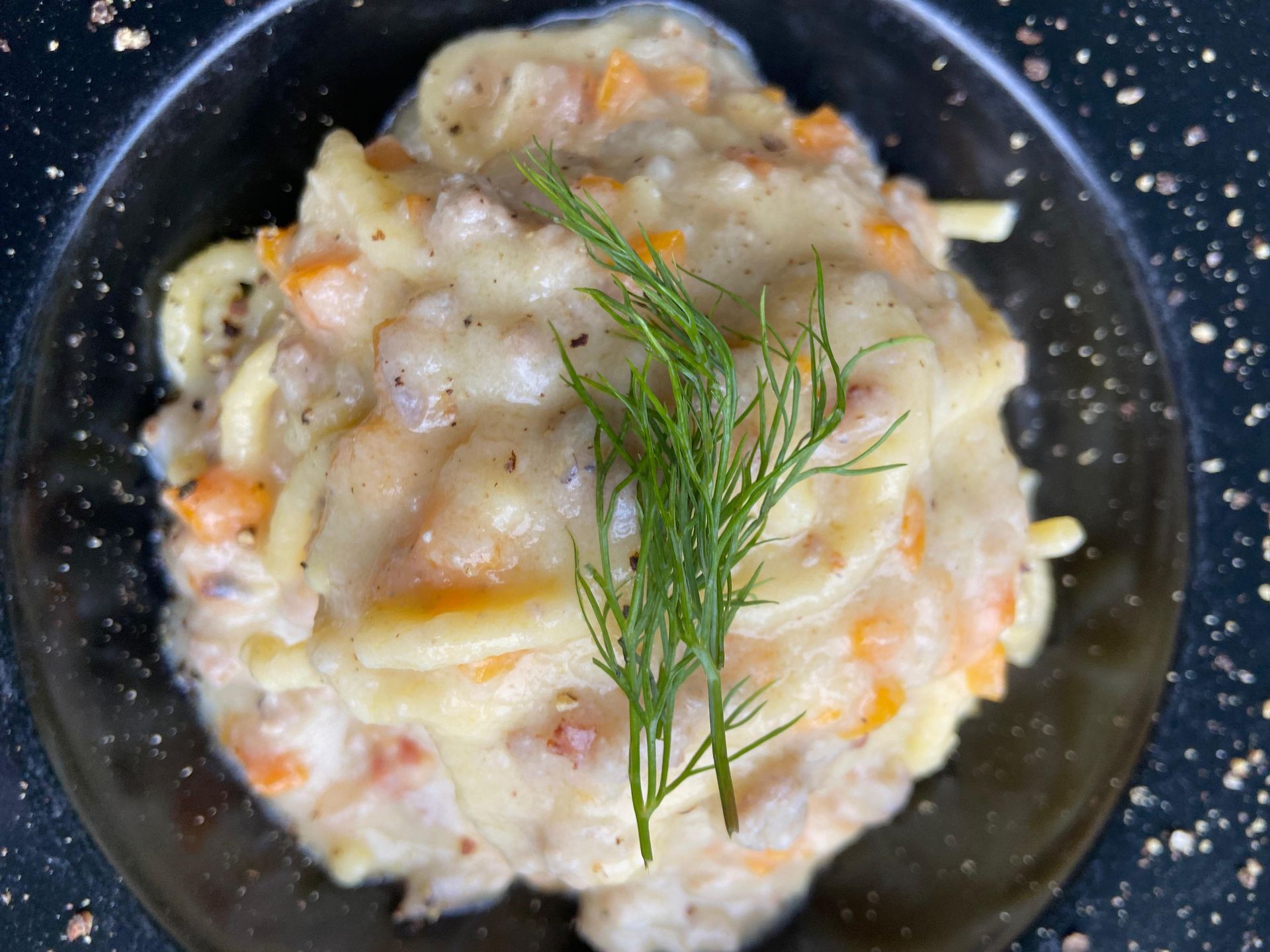 Piatto di pasta con salsa verde, guarnito con besciamella cremosa e pancetta croccante.