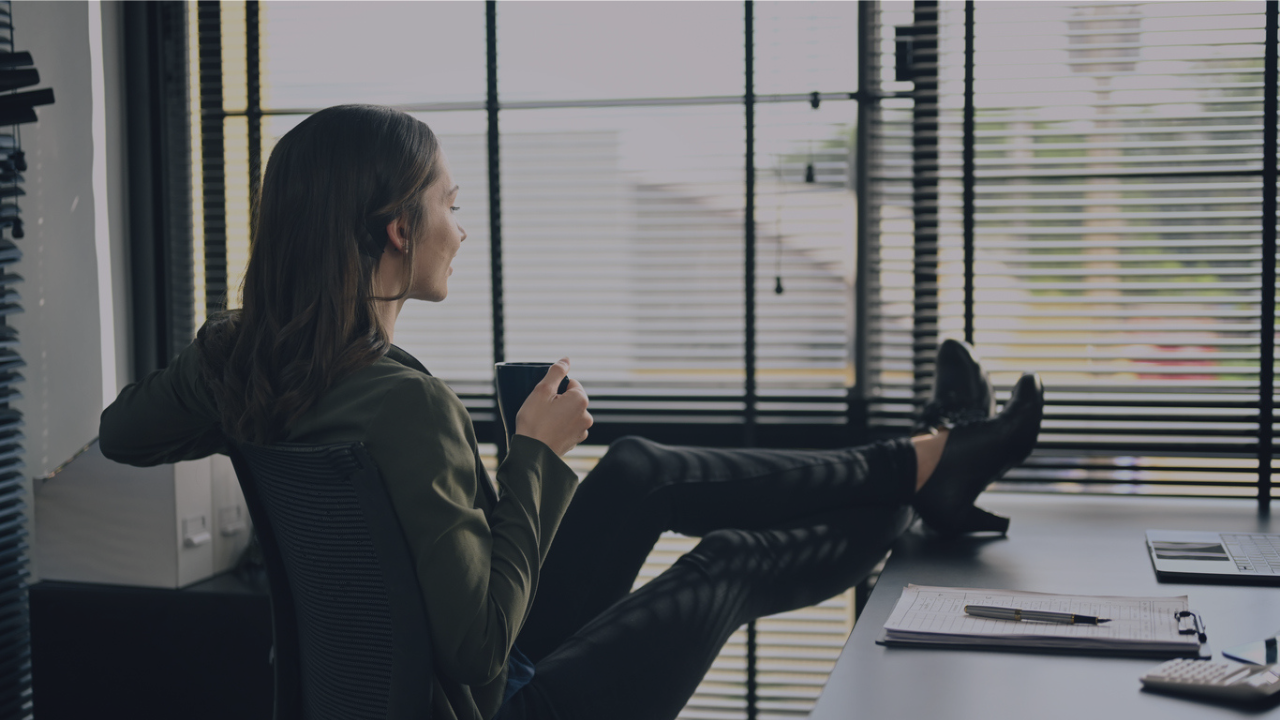 Woman sitting back with feet up on desk drinking coffee, finally organized, found what she needed