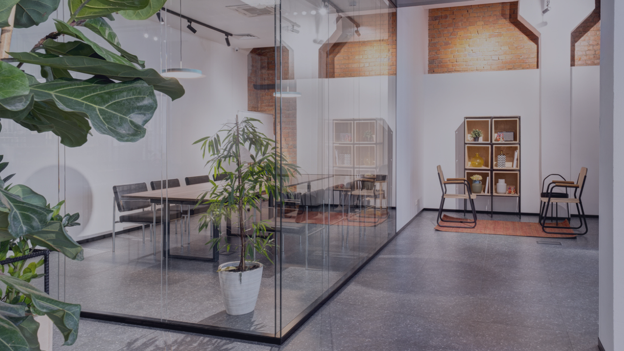 Corporate office with glass wall conference room, open seating area, and indoor plants for wellness