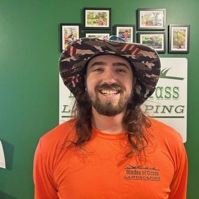 A man with long hair and a beard is wearing a hat and an orange shirt.