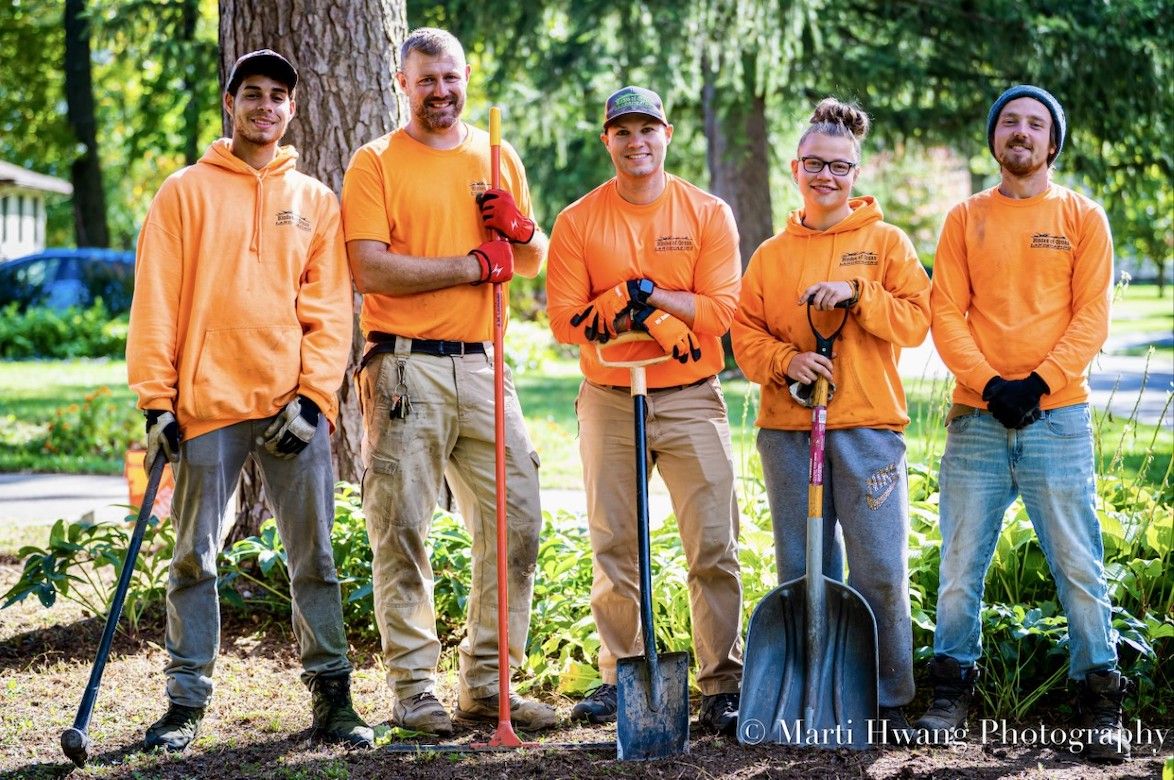 A group of people are standing next to each other in a park holding shovels.