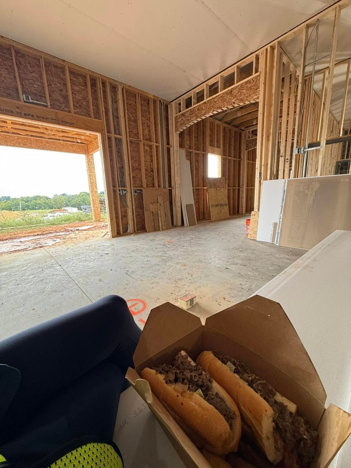 Box of Philly cheesesteaks in a construction site with exposed wood framing.