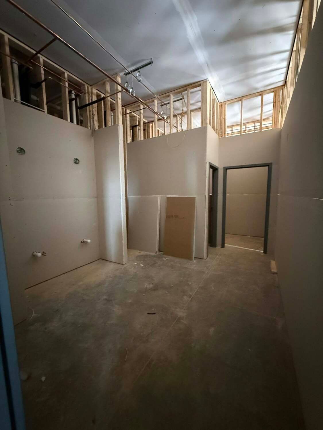 Interior of a room under construction, with exposed wood framing and drywall. Includes a doorway and plumbing.