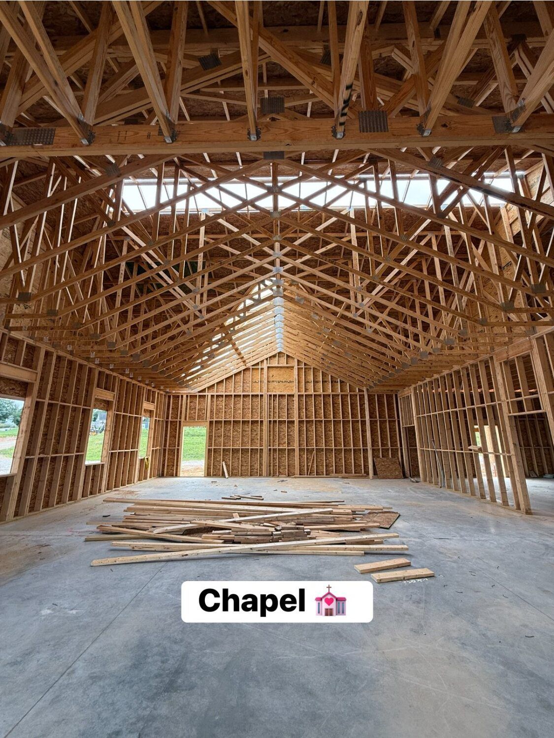 Interior of a chapel under construction; wooden beams frame the walls and arched ceiling. Concrete floor.