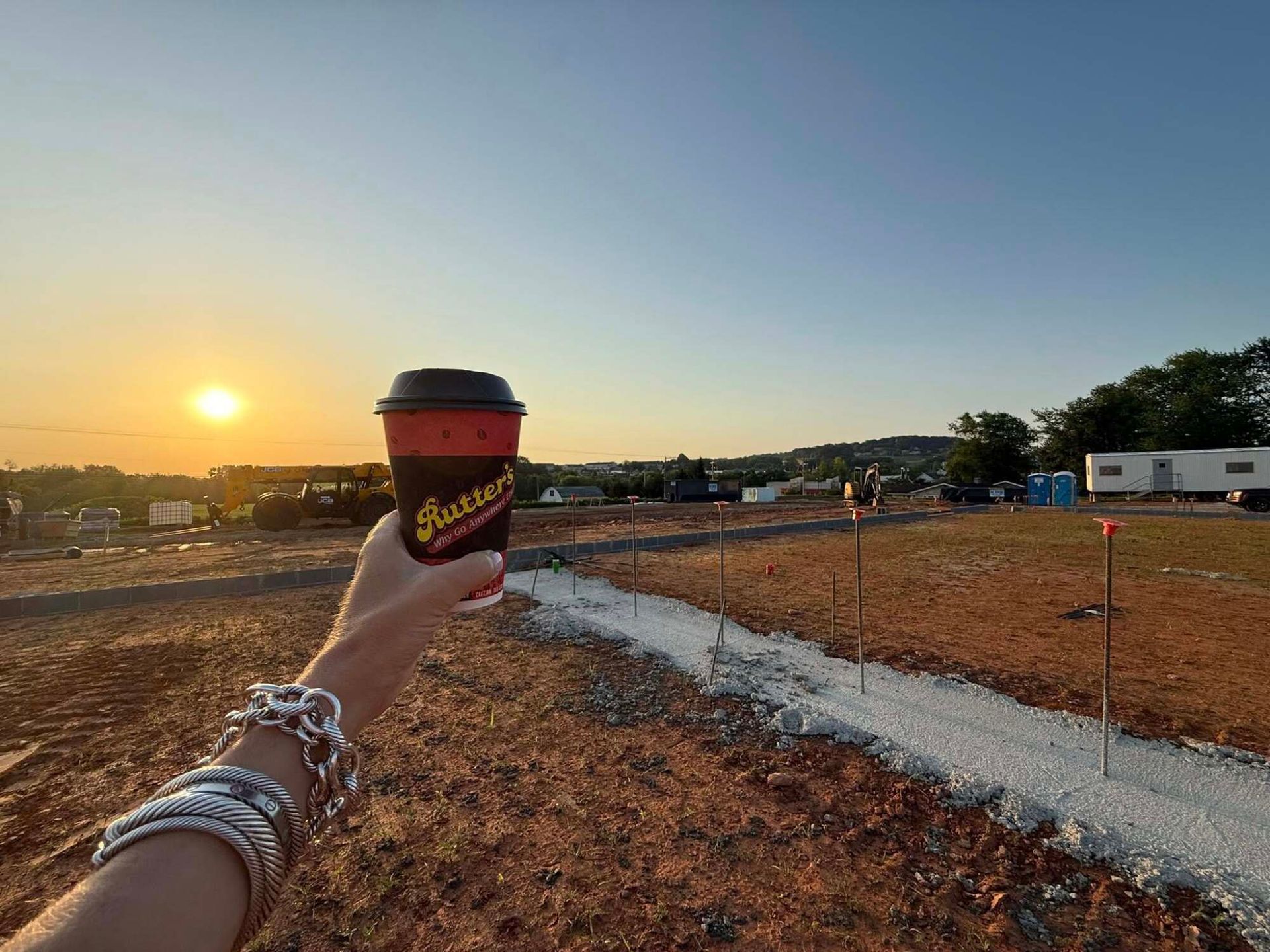 Hand holding a coffee cup, at sunset, over a construction site.
