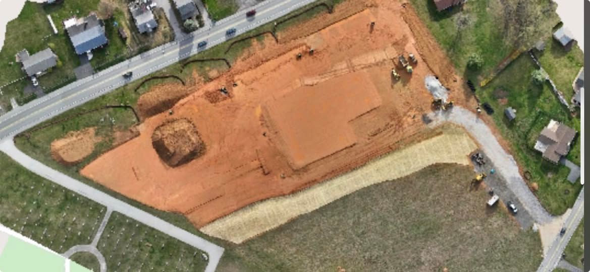 Aerial view of a construction site with exposed red earth, roads, and surrounding houses.