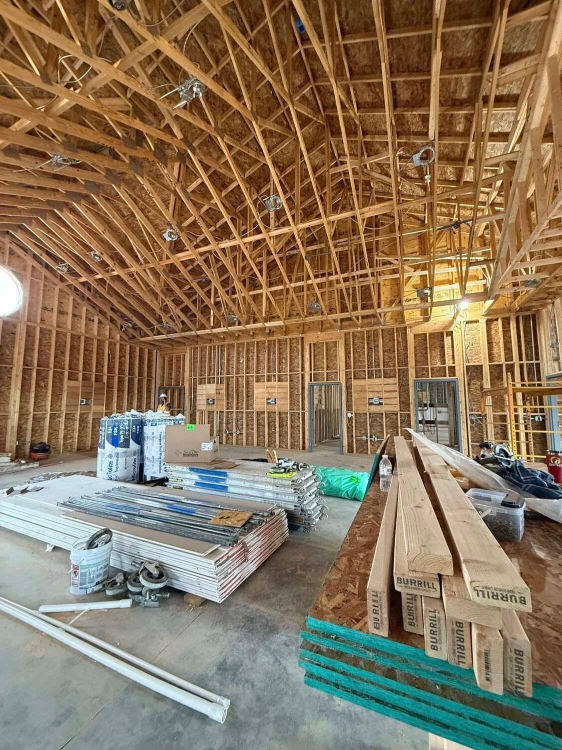 Interior of a wooden building under construction, showing framing, roof supports, and materials stacked on the floor.