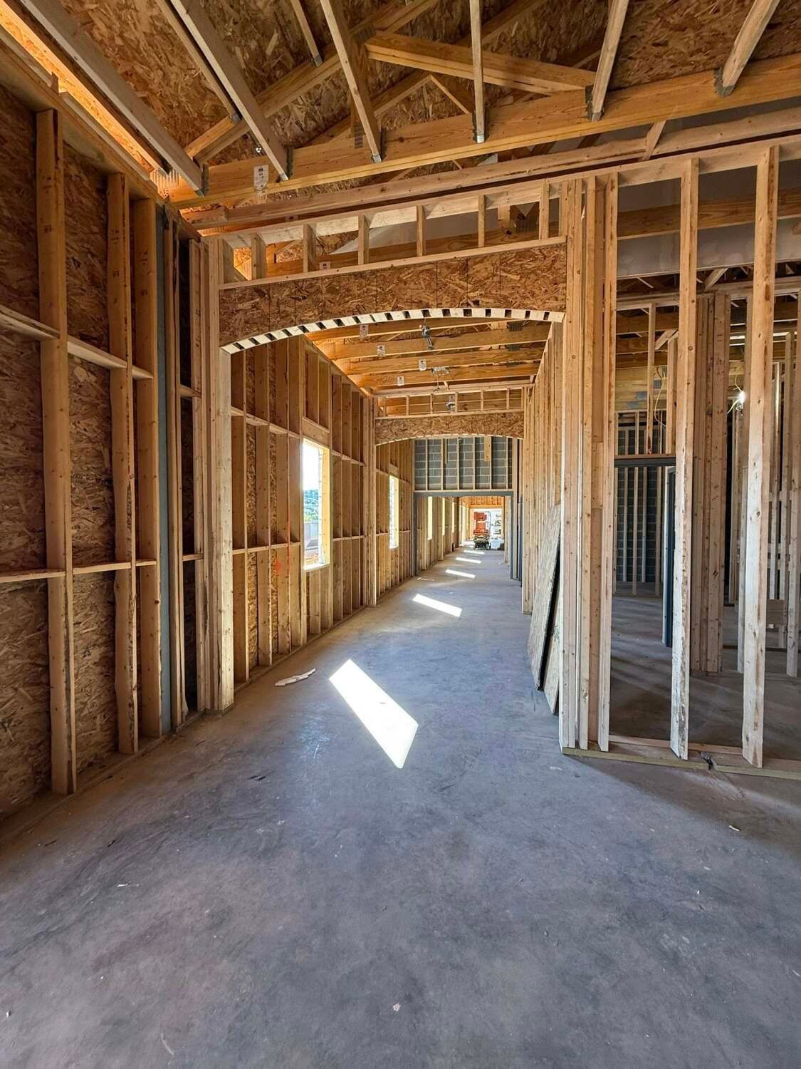 Interior of a building under construction, showing wooden framing and concrete floor. Daylight streams in.