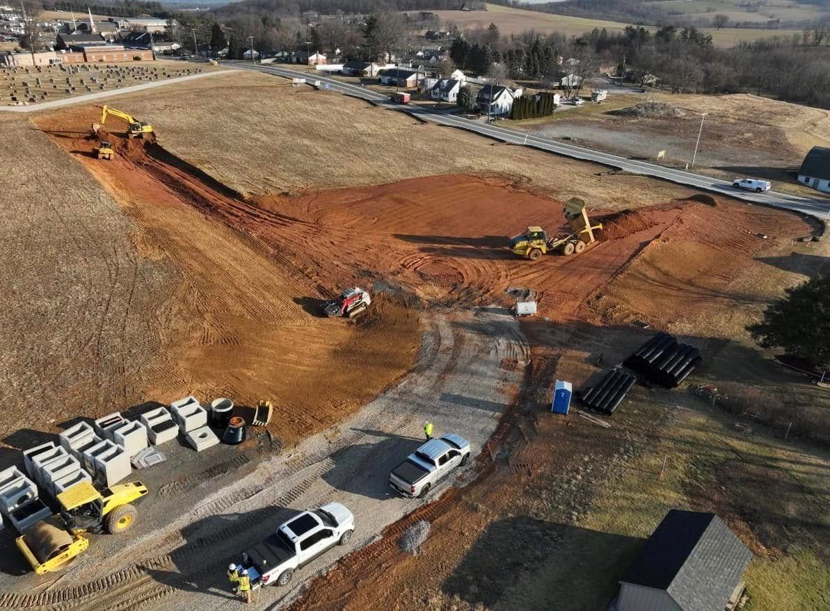 Construction site with excavators, trucks, and materials. Brown earth, blue sky, and rural setting.