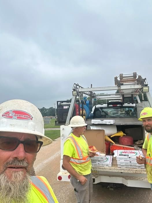Three construction workers eating pizza near a work truck under a cloudy sky.