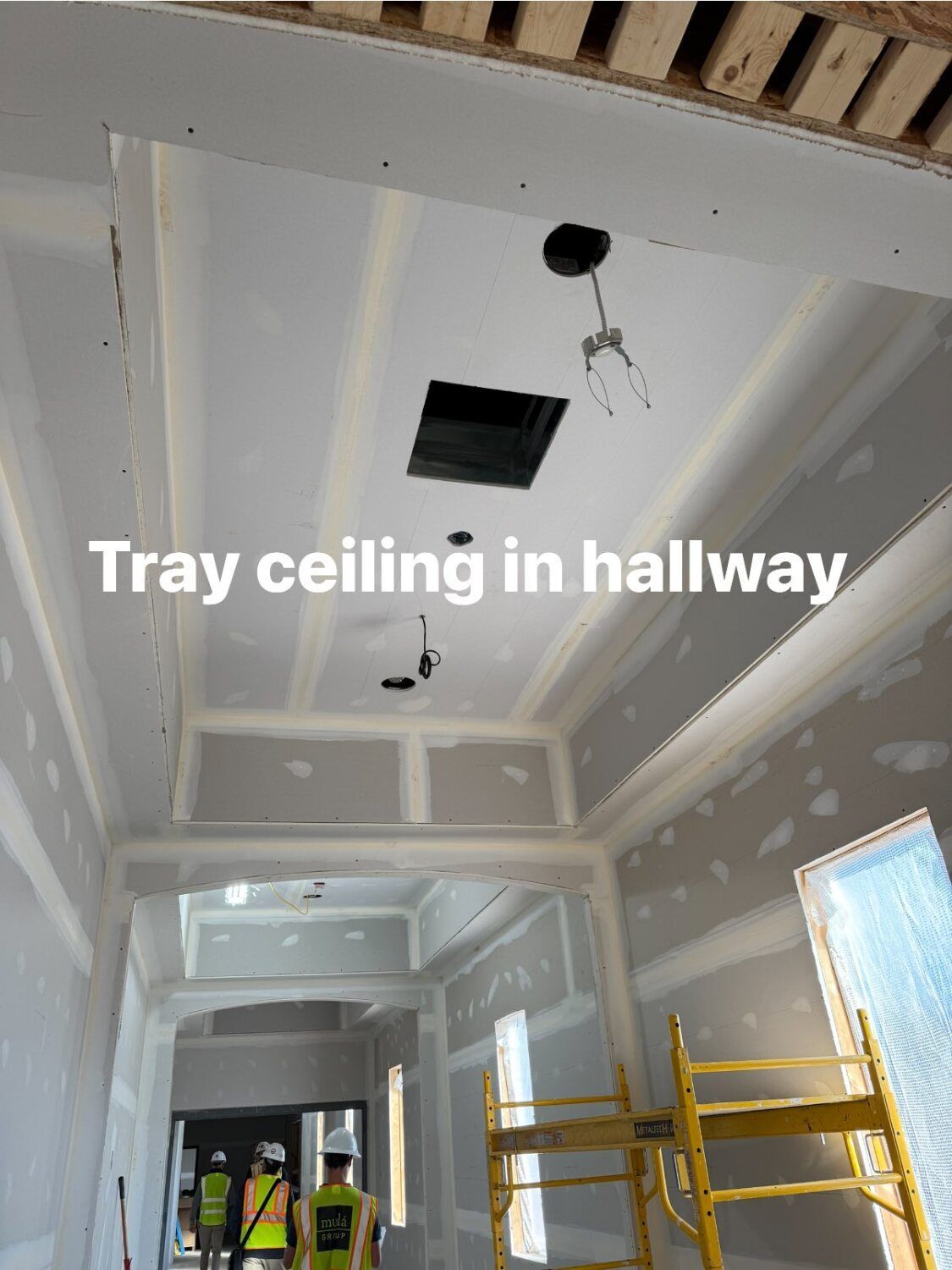 Hallway with unfinished tray ceiling; workers are visible.