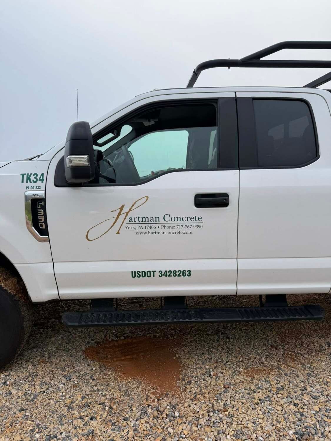 White Ford pickup truck with black roof rack and company logo on the side.