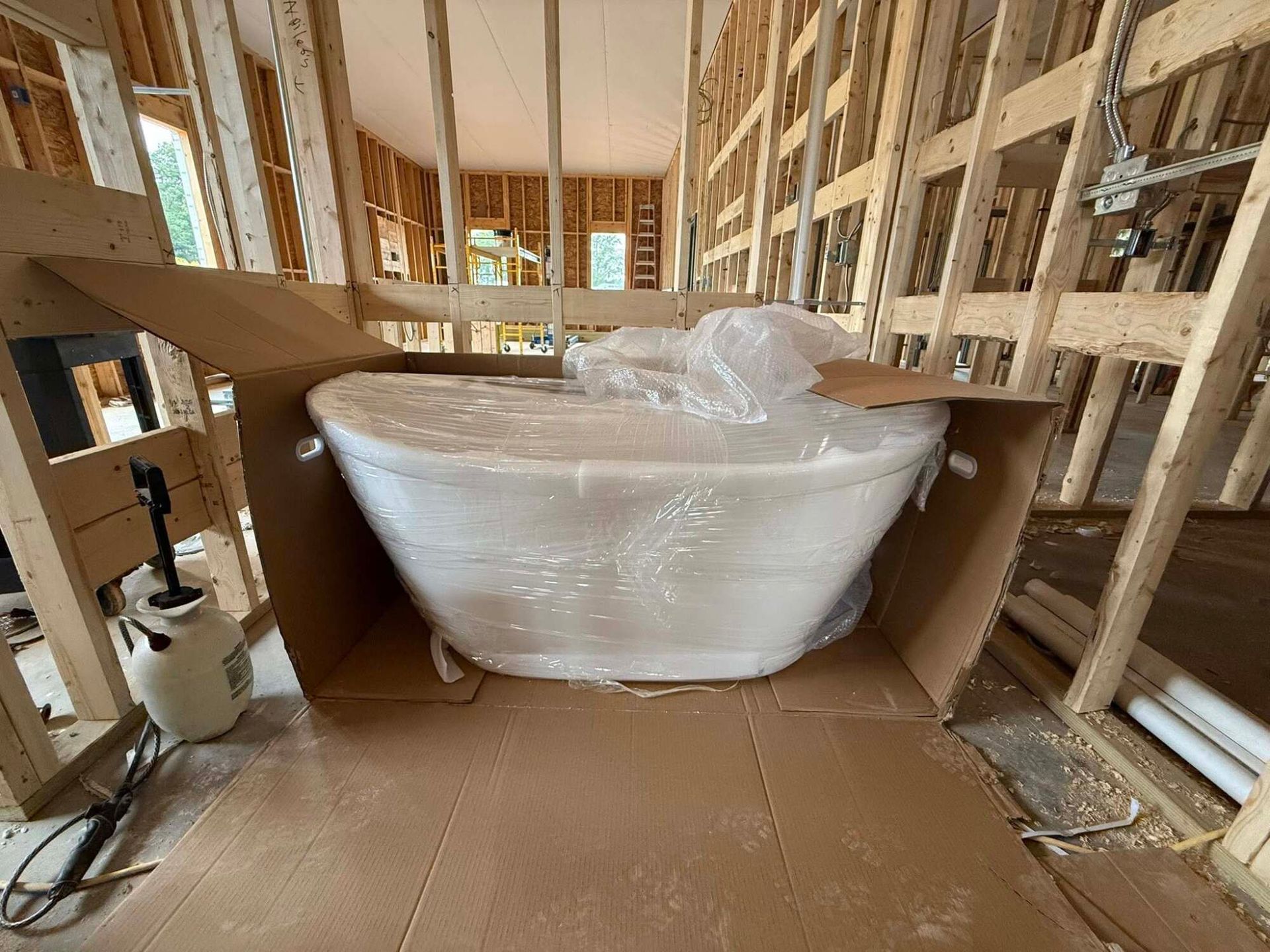Bathtub, still wrapped in plastic, inside cardboard box, in a house under construction.