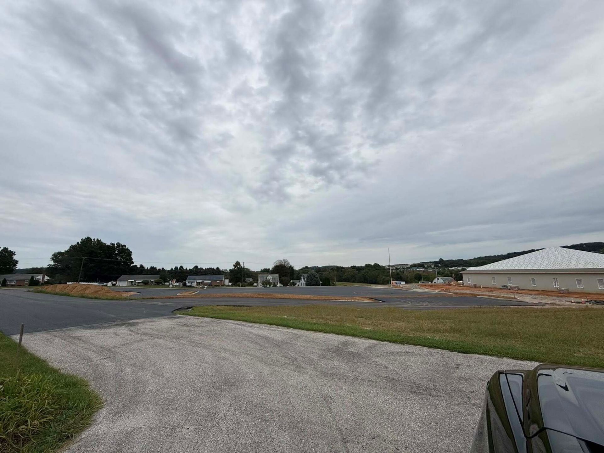 Gravel driveway leads to a grassy field with construction; cloudy sky overhead.