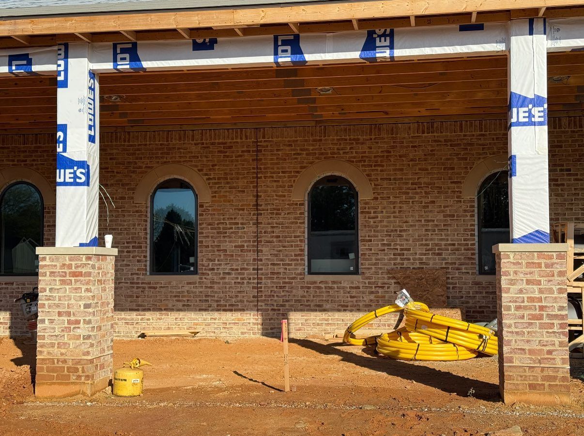 Brick house under construction with arched windows and porch pillars.