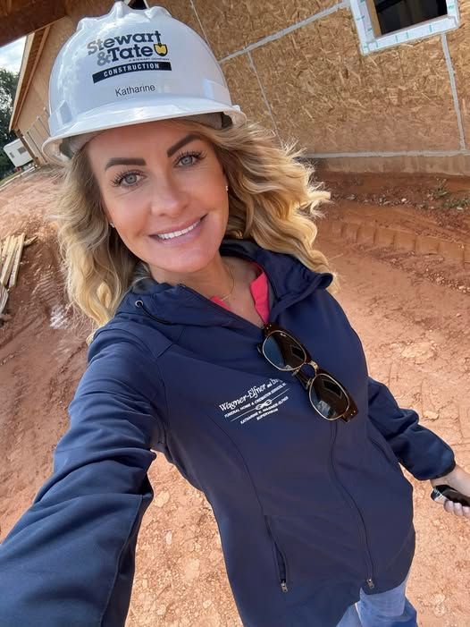 Woman in hard hat and jacket smiles on a construction site.