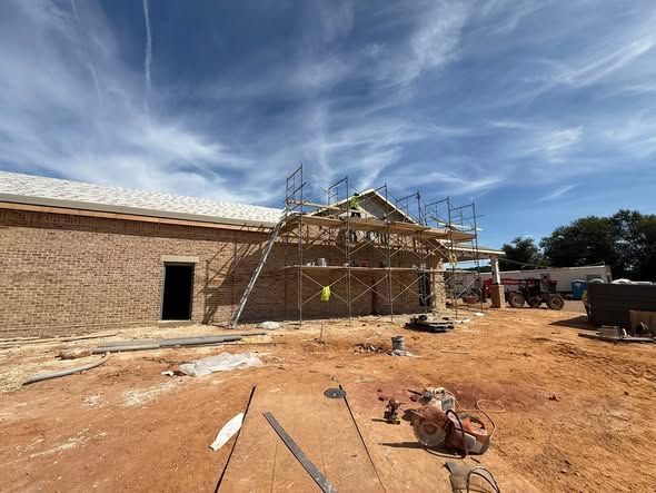 Construction site; building with scaffolding, exposed framing, and open doorway, under a blue sky.