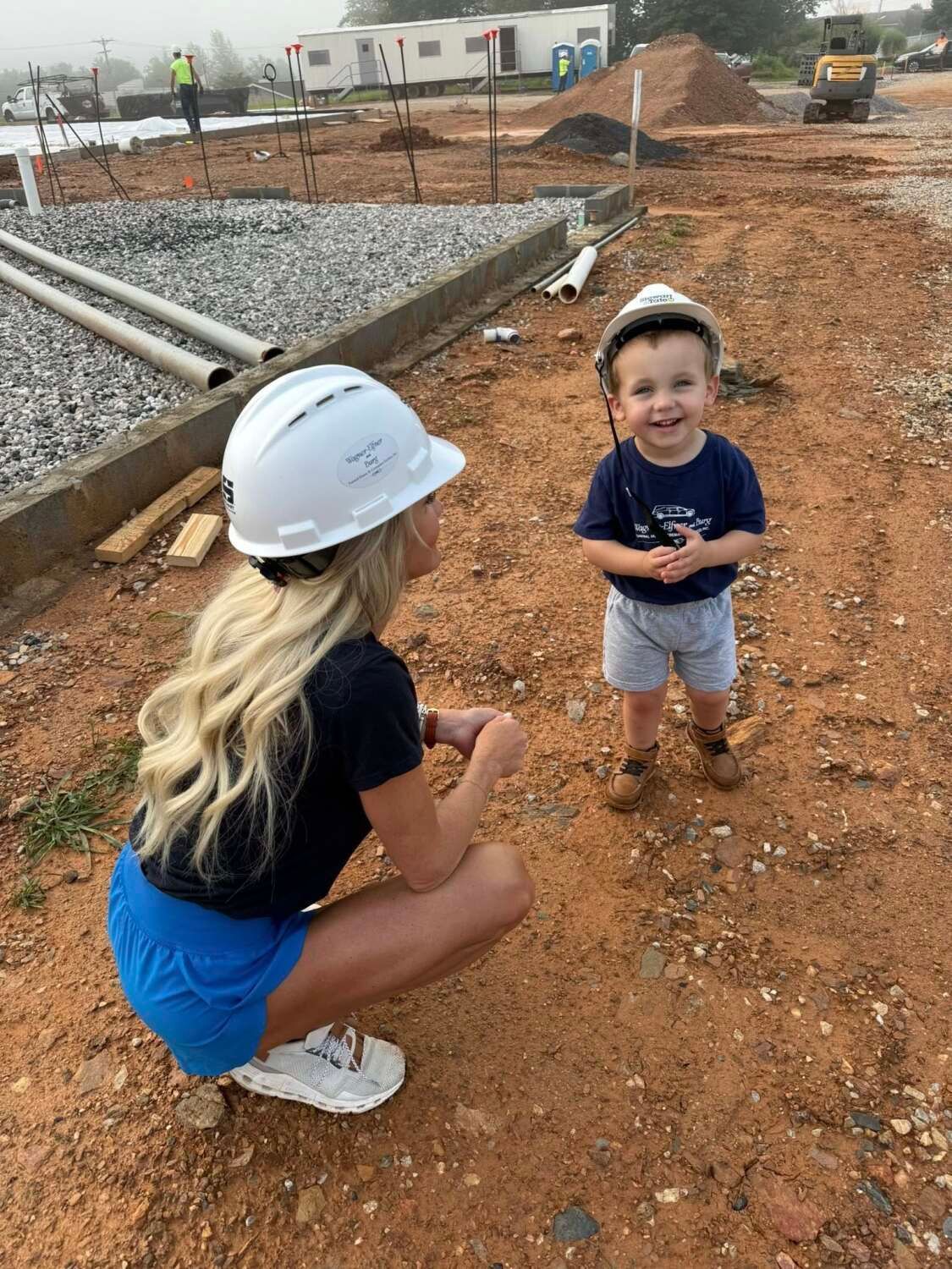 Woman and child wearing construction helmets on a construction site. Child is smiling.