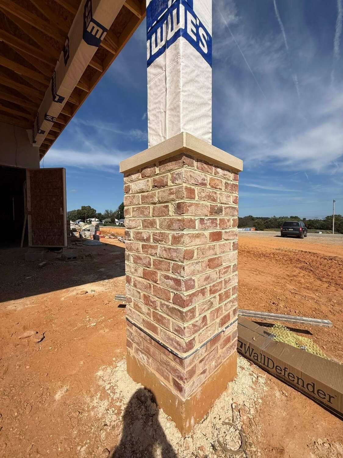 Brick pillar with a stone cap at a construction site, Lowe's signage in the background.