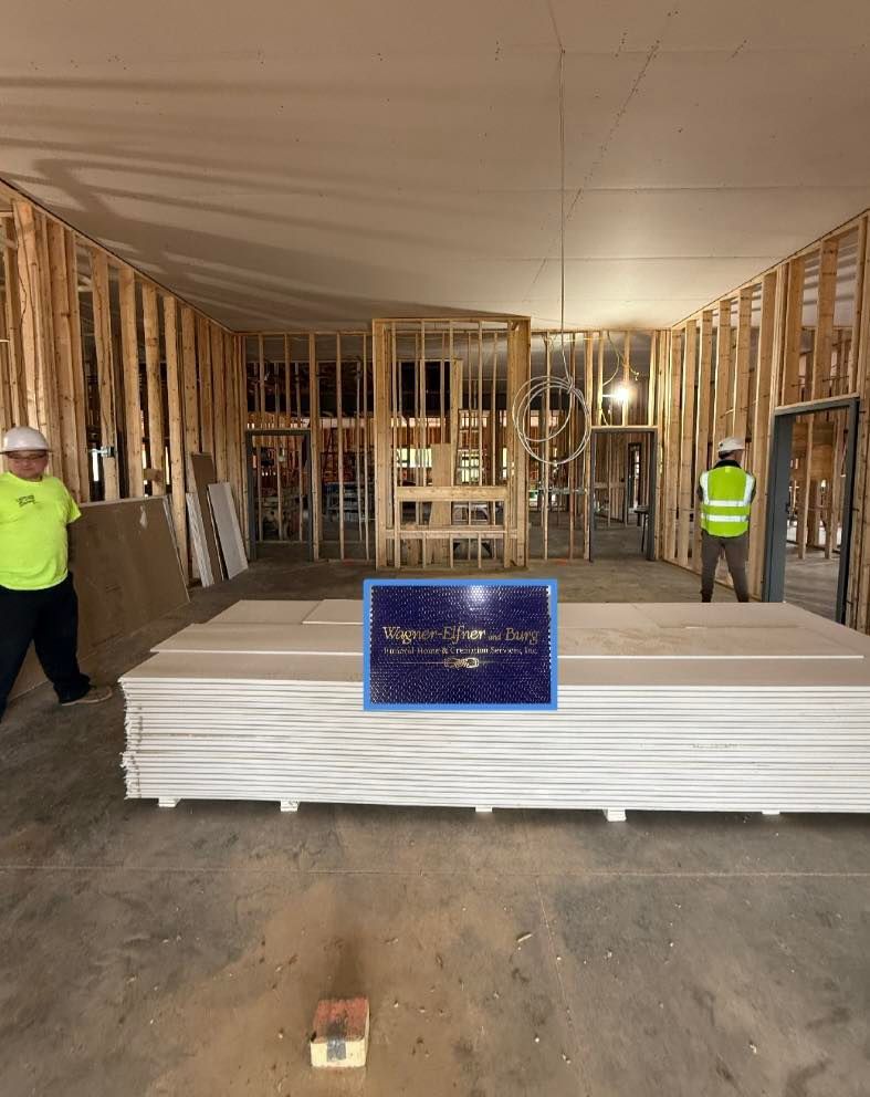 Construction site interior with workers, wood framing, drywall stack, and a plaque.