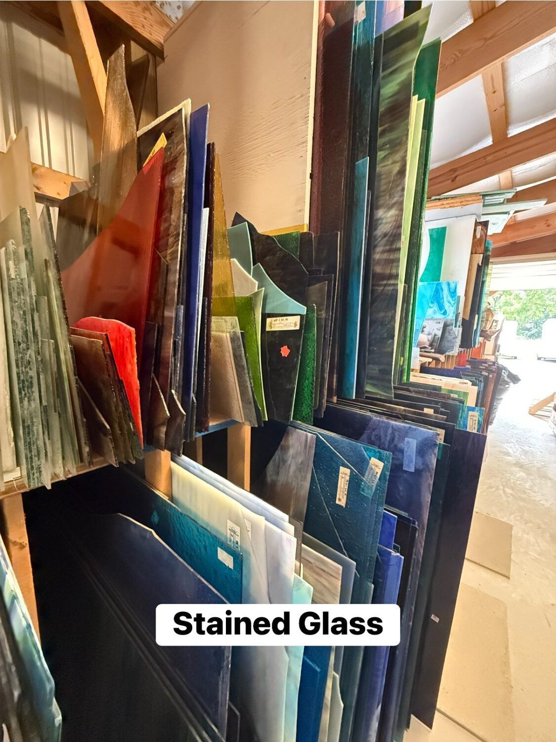 Shelves filled with various colored stained glass sheets in a workshop setting.