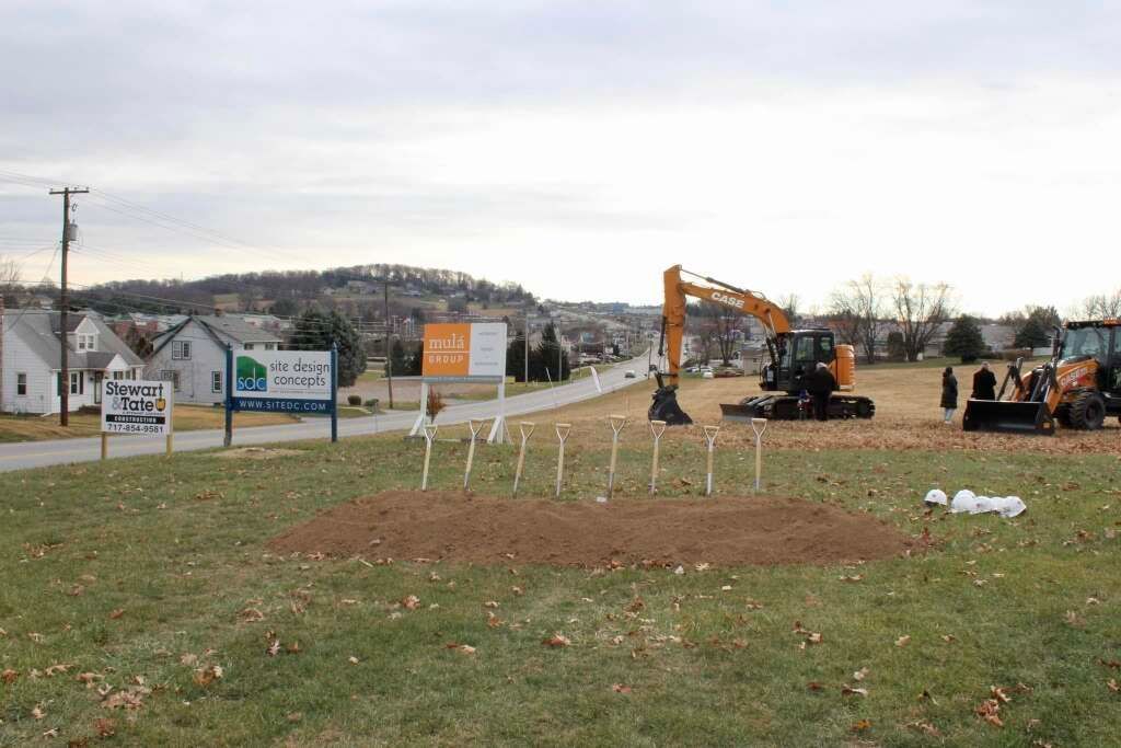 Construction site with earth mounds and machinery near signs and residential buildings.